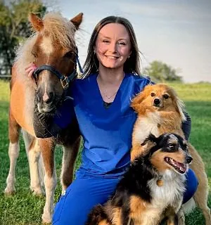 Female kneeling down beside a mini pony and 12 medium sized dogs