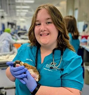 Female wearing teal scrubs and holding a newborn puppy
