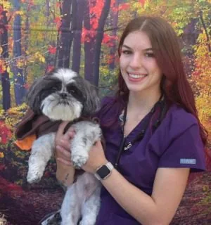 female wearing a purple v-neck shirt holding a maltese